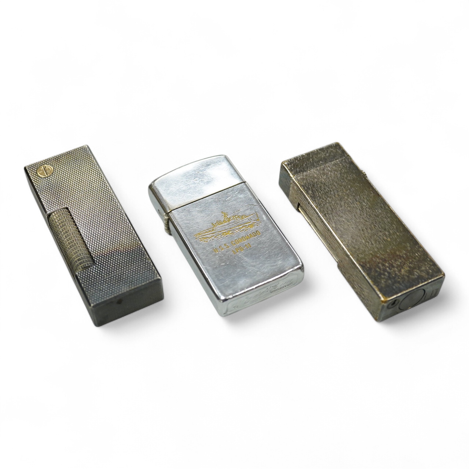 Two Dunhill rollagas silver plated lighters, barley pattern and rusticated 6.5cm long and a U.S.S. Coronado LPD-11, zippo lighter (3)